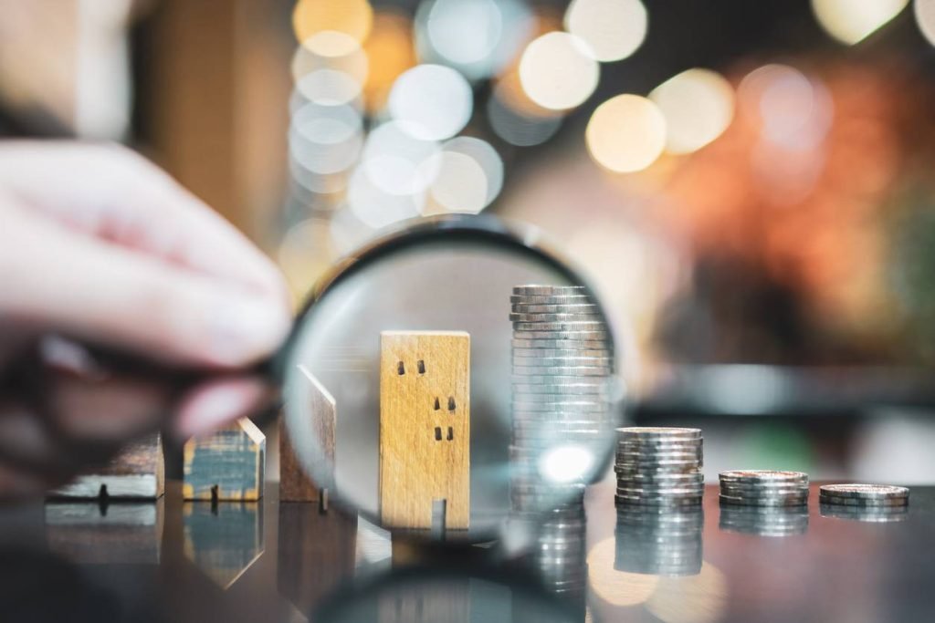 Photo d'une loupe qui zoome sur un immeuble et des pièces de monnaie