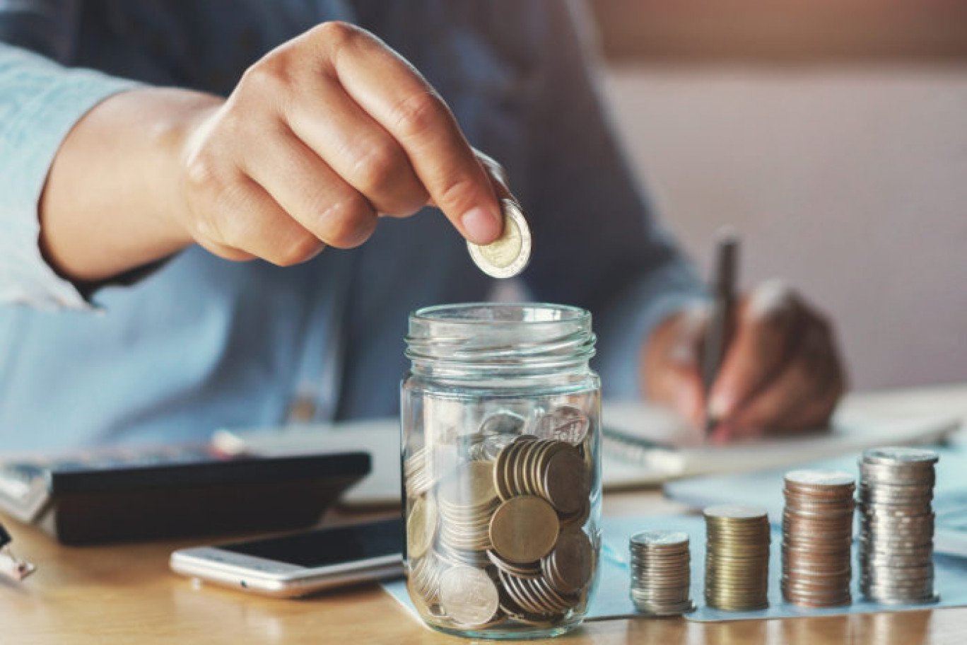 Photo d'une personne qui tient ses comptes. Il y a 4 piles de pièces classées par taille et un pot en verre rempli de pièces.