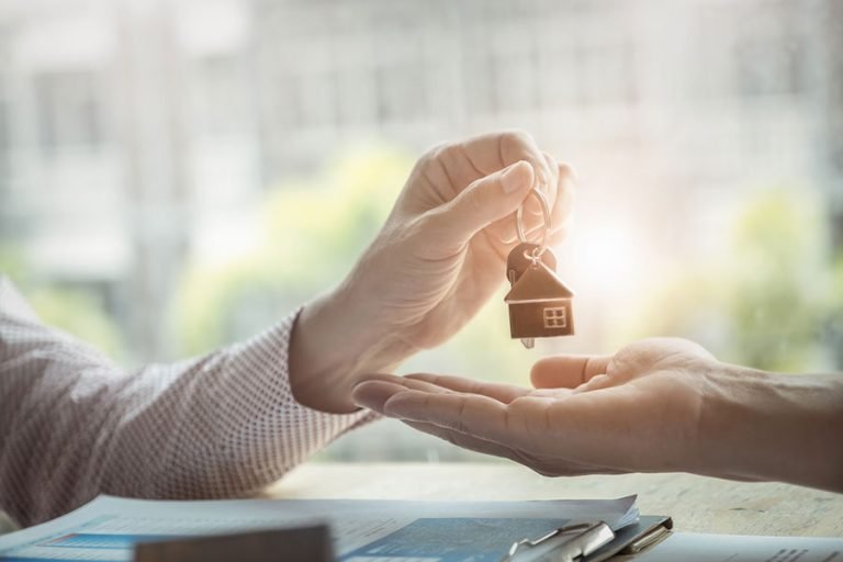 Un main tend une clé avec une maison en porte-clé à une autre main qui la reçoit.